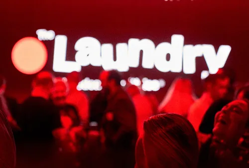 People socializing in a dimly lit venue with a large illuminated ‘Laundry’ sign in the background.