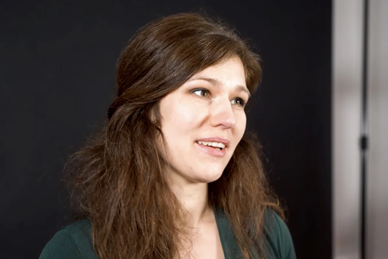 Smiling woman with long brown hair looking slightly upward against a dark background.