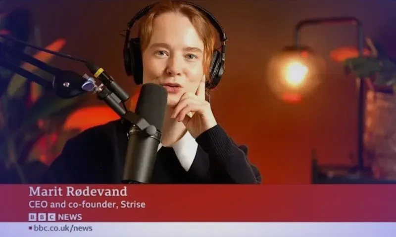 Marit Rødevand, CEO and co-founder of Strise, speaking into a microphone while wearing headphones in a studio with warm lighting.